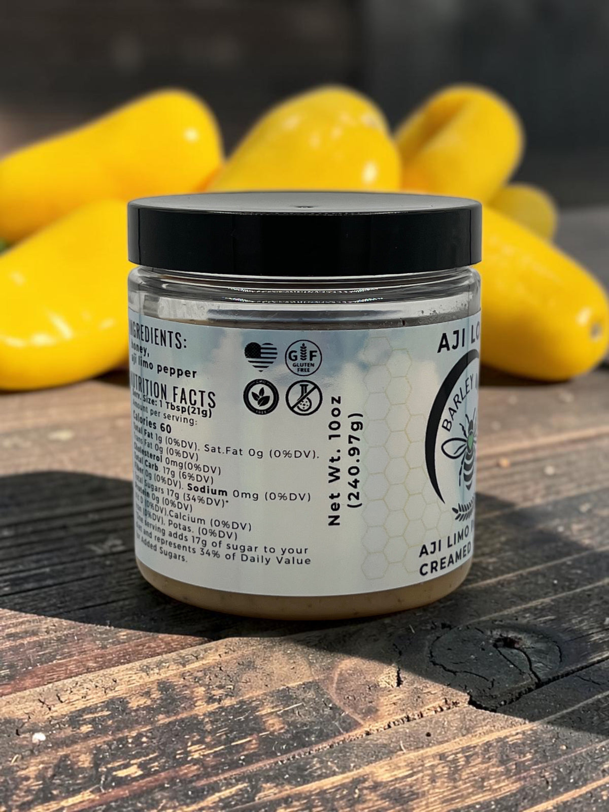 Barley Moon Botanicals Aji Limo Creamed Honey jar with nutrition label, set against a background of yellow Aji peppers.
