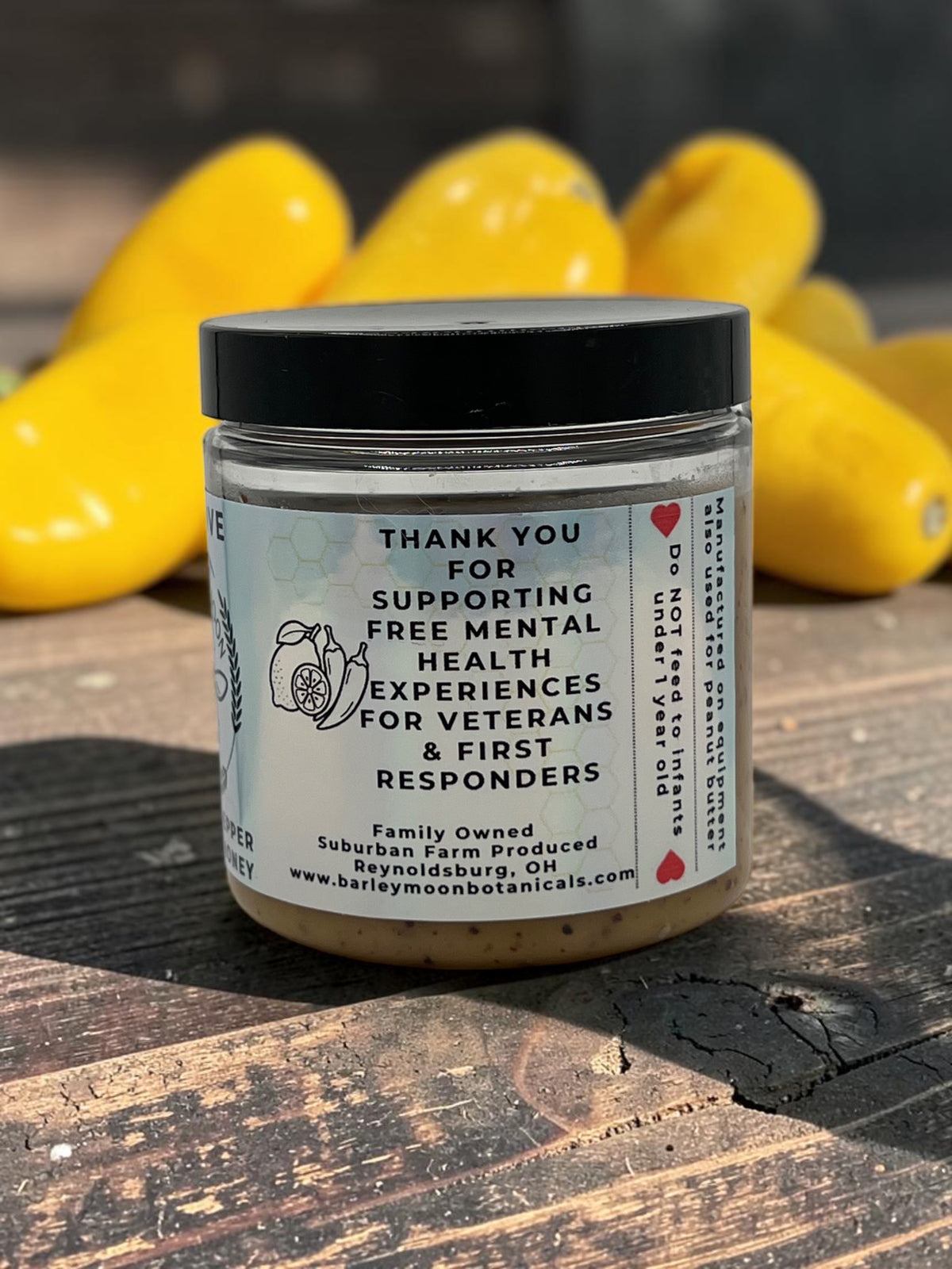 Barley Moon Botanicals Aji Limo creamed honey jar with yellow peppers in the background on a wooden surface.