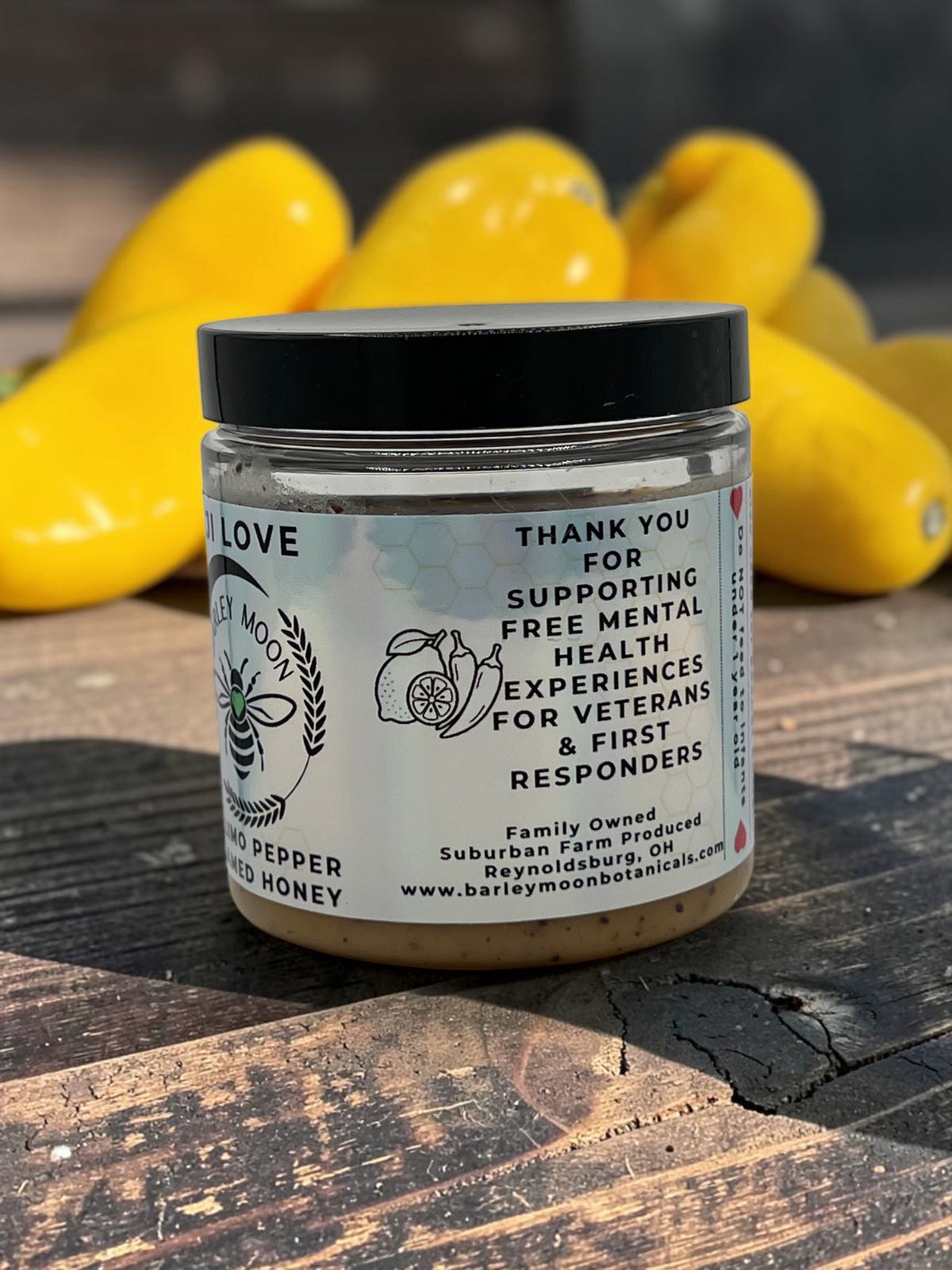 Barley Moon Botanicals Aji Limo creamed honey jar with a black lid, displayed in front of fresh yellow Aji Limo peppers.