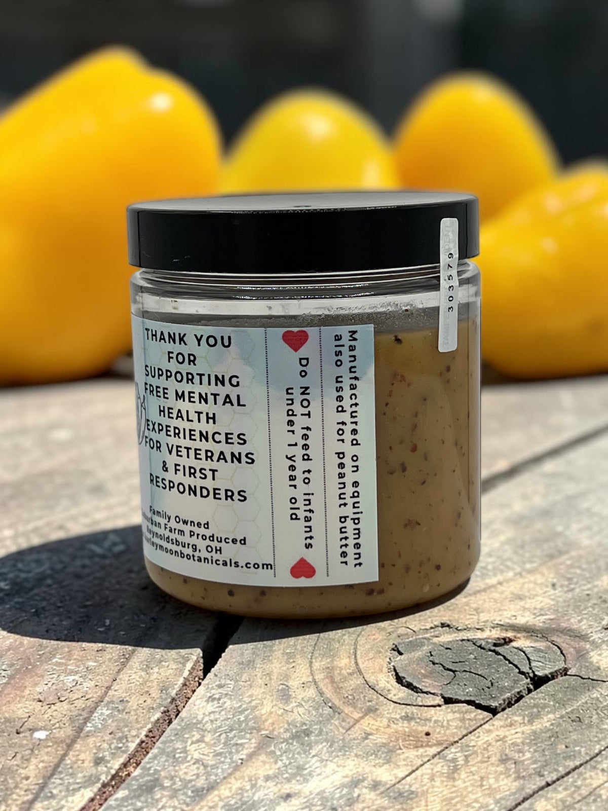 Barley Moon Botanicals Aji Limo creamed honey in a clear jar with a black lid, set against yellow bell peppers.