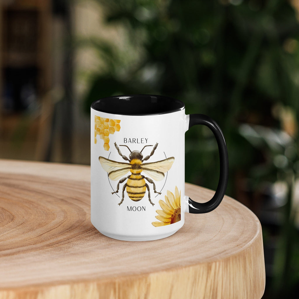 Barley Moon Botanicals 15oz ceramic mug with bee and flower design, black handle and interior on a wooden table.