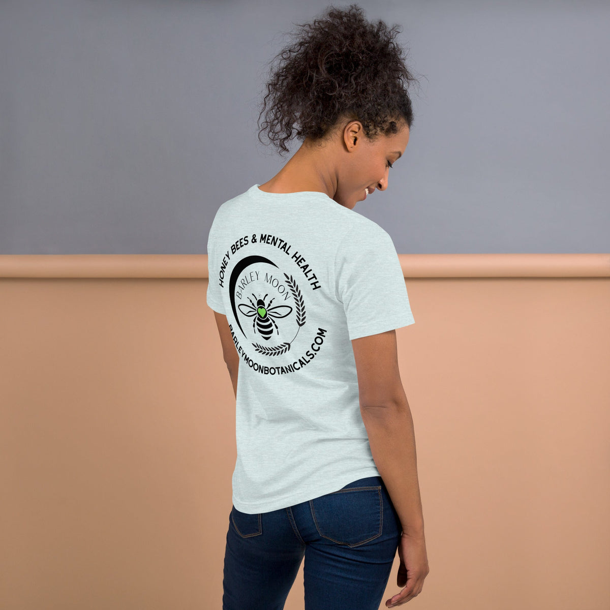 Woman wearing a light blue Barley Moon Botanicals t-shirt with a black bee and crescent moon logo on the back
