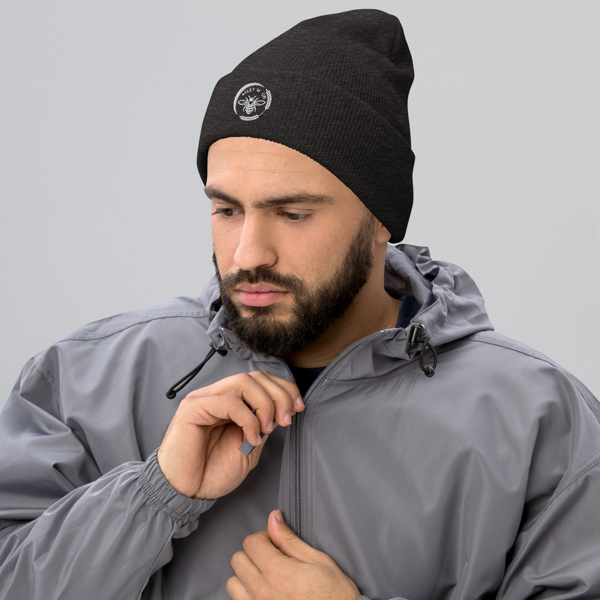 Barley Moon Botanicals black cuffed beanie with white bee and moon logo worn by a man in a grey jacket.