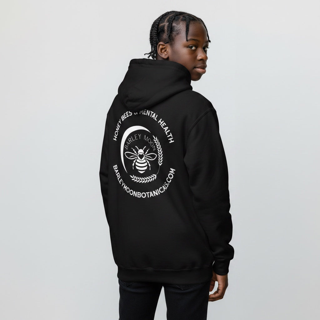 A person wearing a black Barley Moon Botanicals unisex hoodie with a white bee and crescent moon logo on the back.