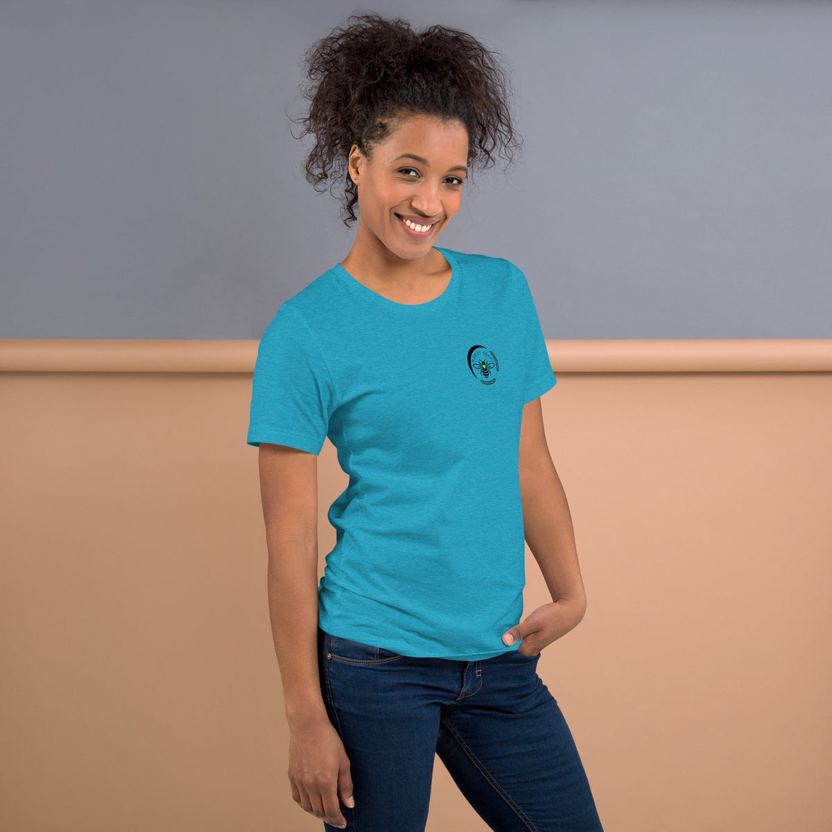 A woman wearing a bright blue Barley Moon Botanicals t-shirt with a small black bee and crescent moon logo on the chest.