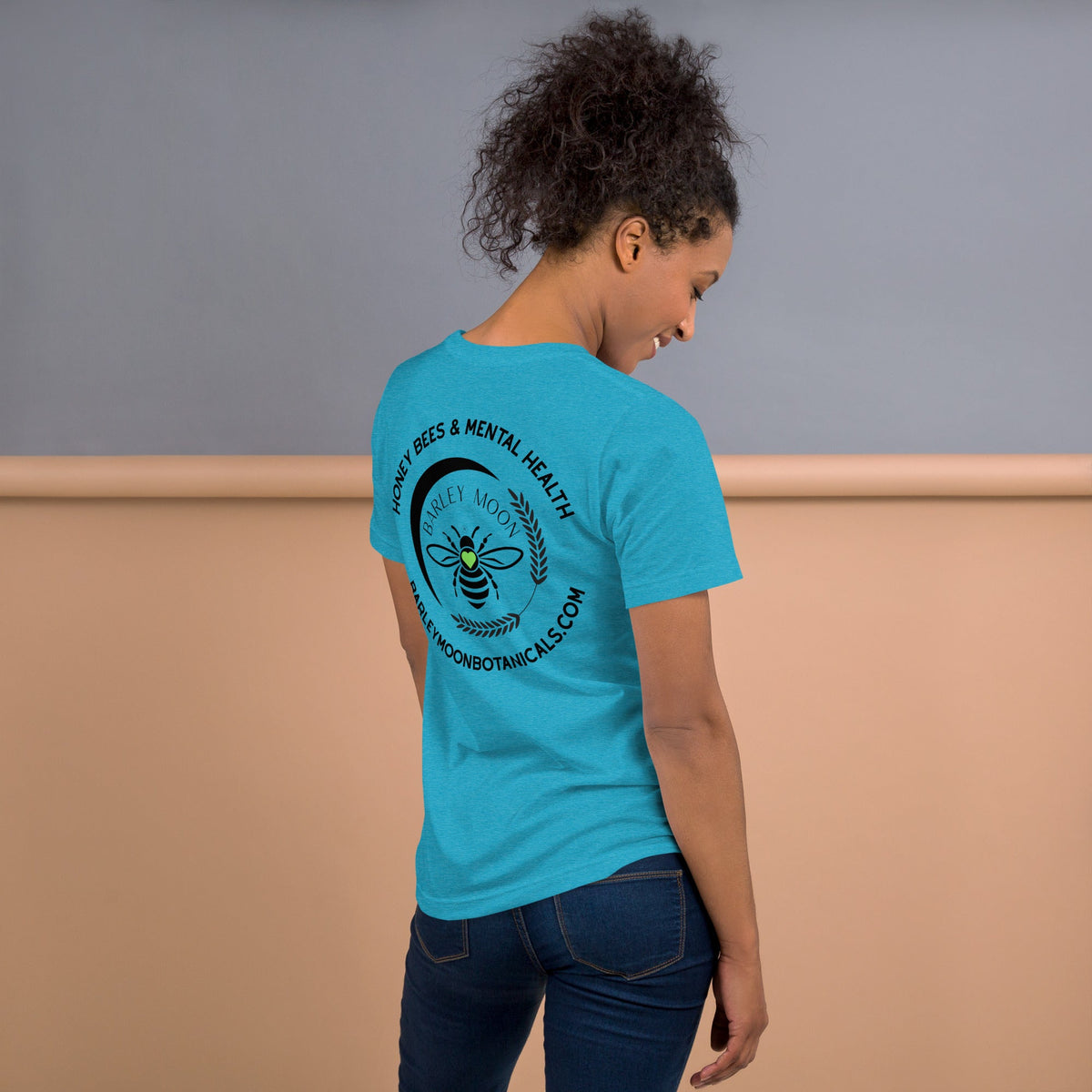 Woman wearing a blue Barley Moon Botanicals t-shirt with a black bee and crescent moon logo on the back