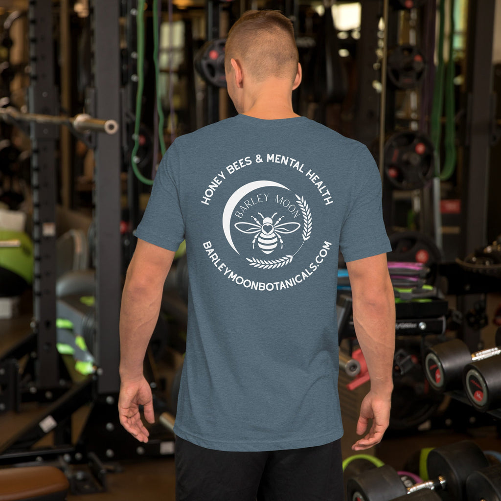 A man wearing a blue Barley Moon Botanicals t-shirt with a white bee and crescent moon logo on the back in a gym.