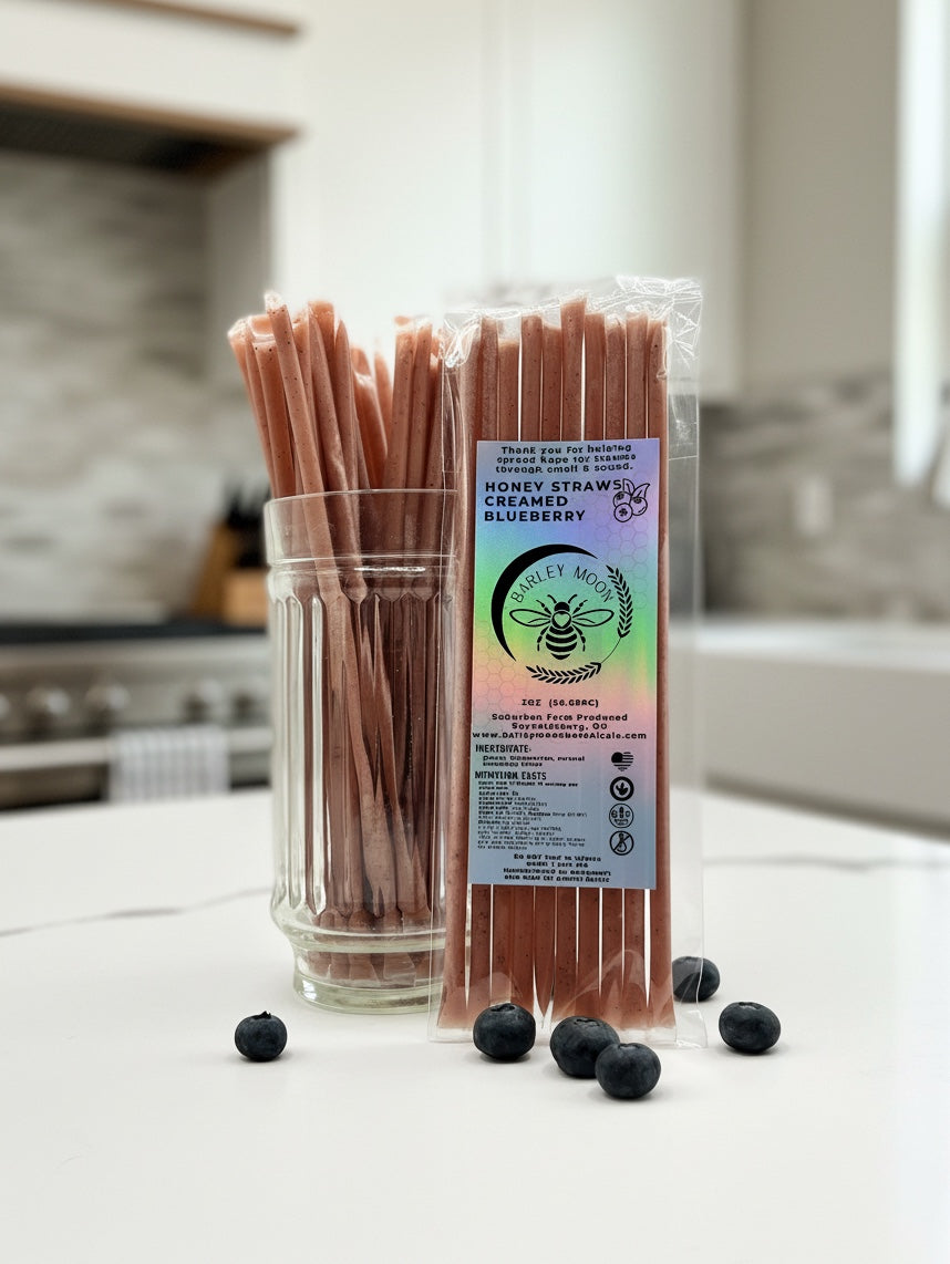 Barley Moon Botanicals blueberry creamed honey straws in a glass jar with fresh blueberries on a white kitchen counter.