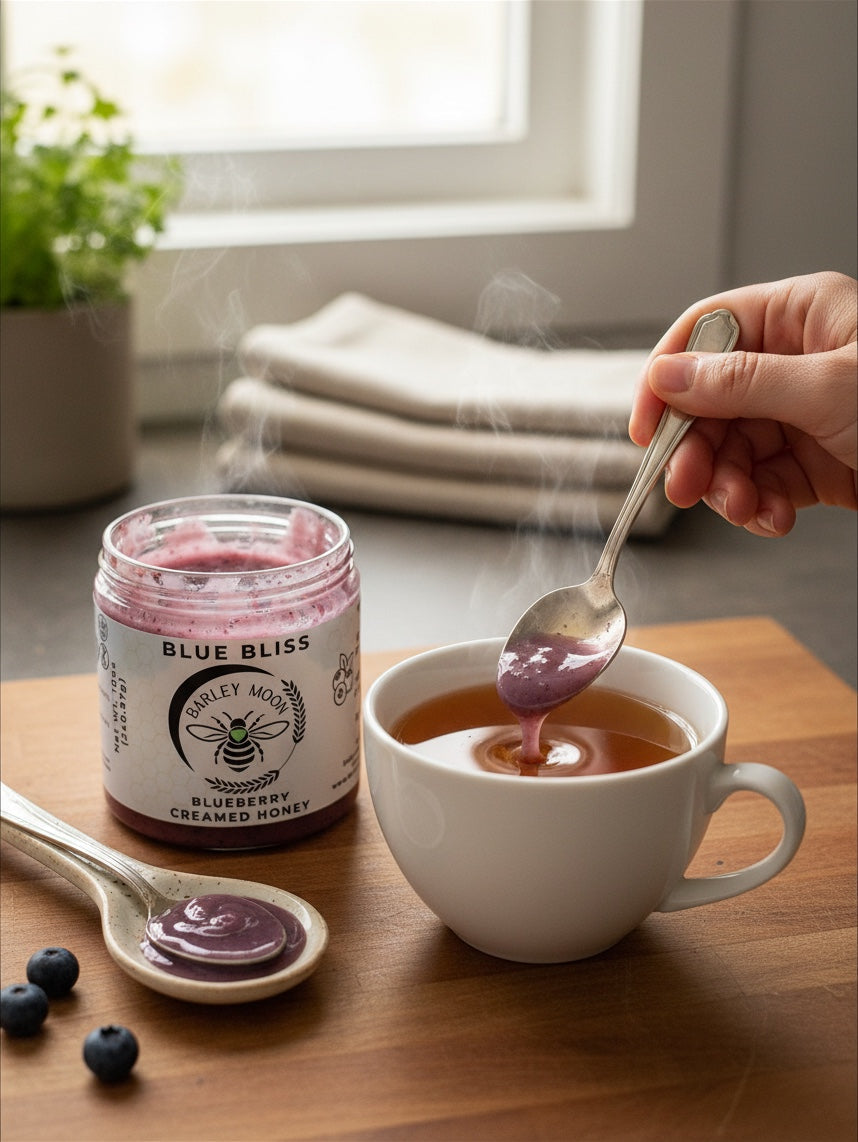 Barley Moon Botanicals Blue Bliss blueberry creamed honey being stirred into a steaming cup of tea on a wooden board