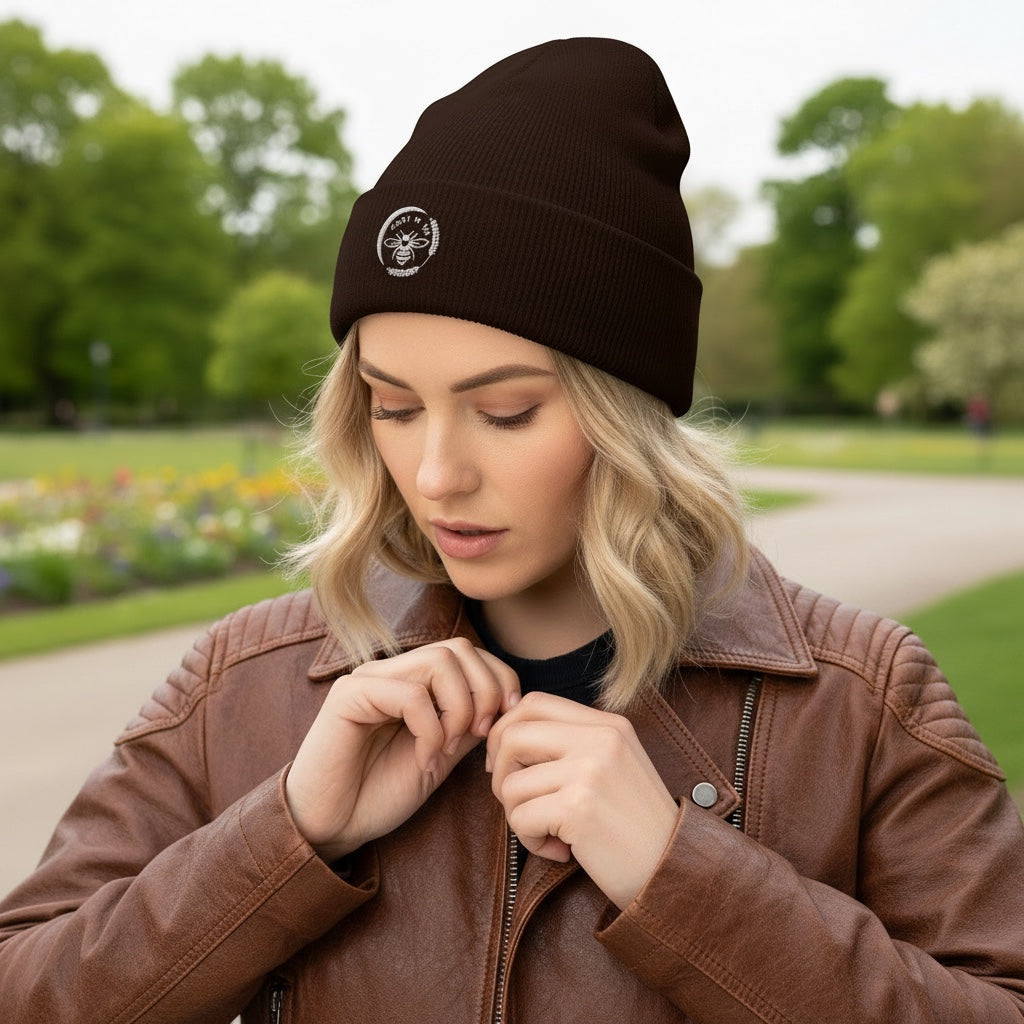 Woman wearing a dark brown Barley Moon Botanicals cuffed beanie with a white bee and moon logo in a park setting.