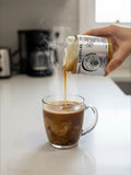 Barley Moon Botanicals Caramel Cuddles creamed honey being poured into a steaming mug of coffee on a kitchen counter.