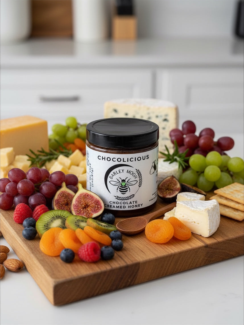 Barley Moon Botanicals Chocolicious chocolate creamed honey jar on a charcuterie board with fruit, cheese, and crackers