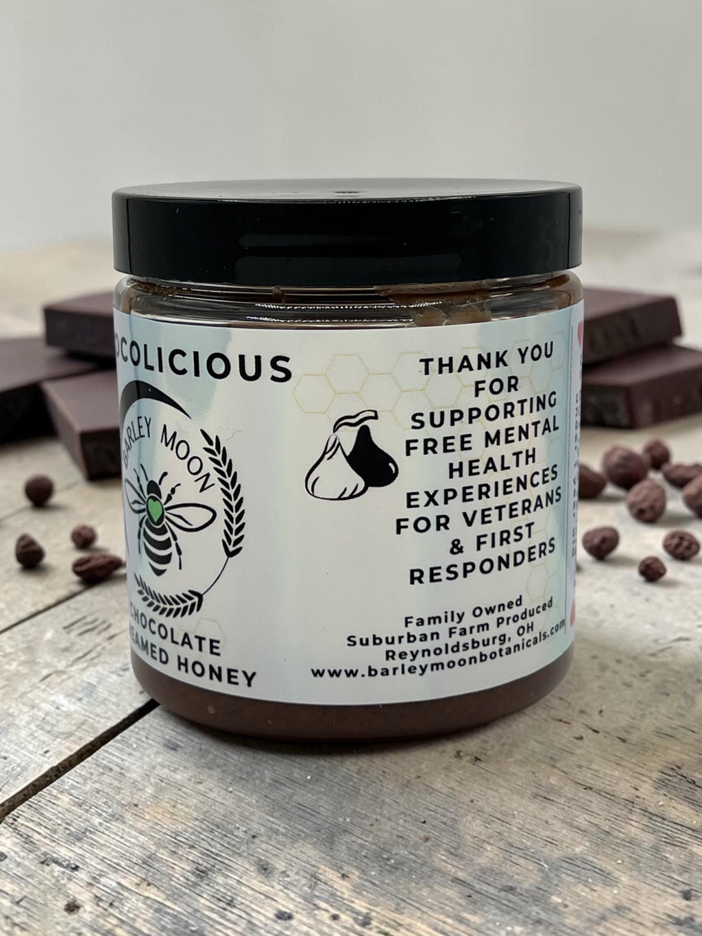 Barley Moon Botanicals Chocolicious chocolate creamed honey jar on a rustic wooden surface with dark chocolate pieces.