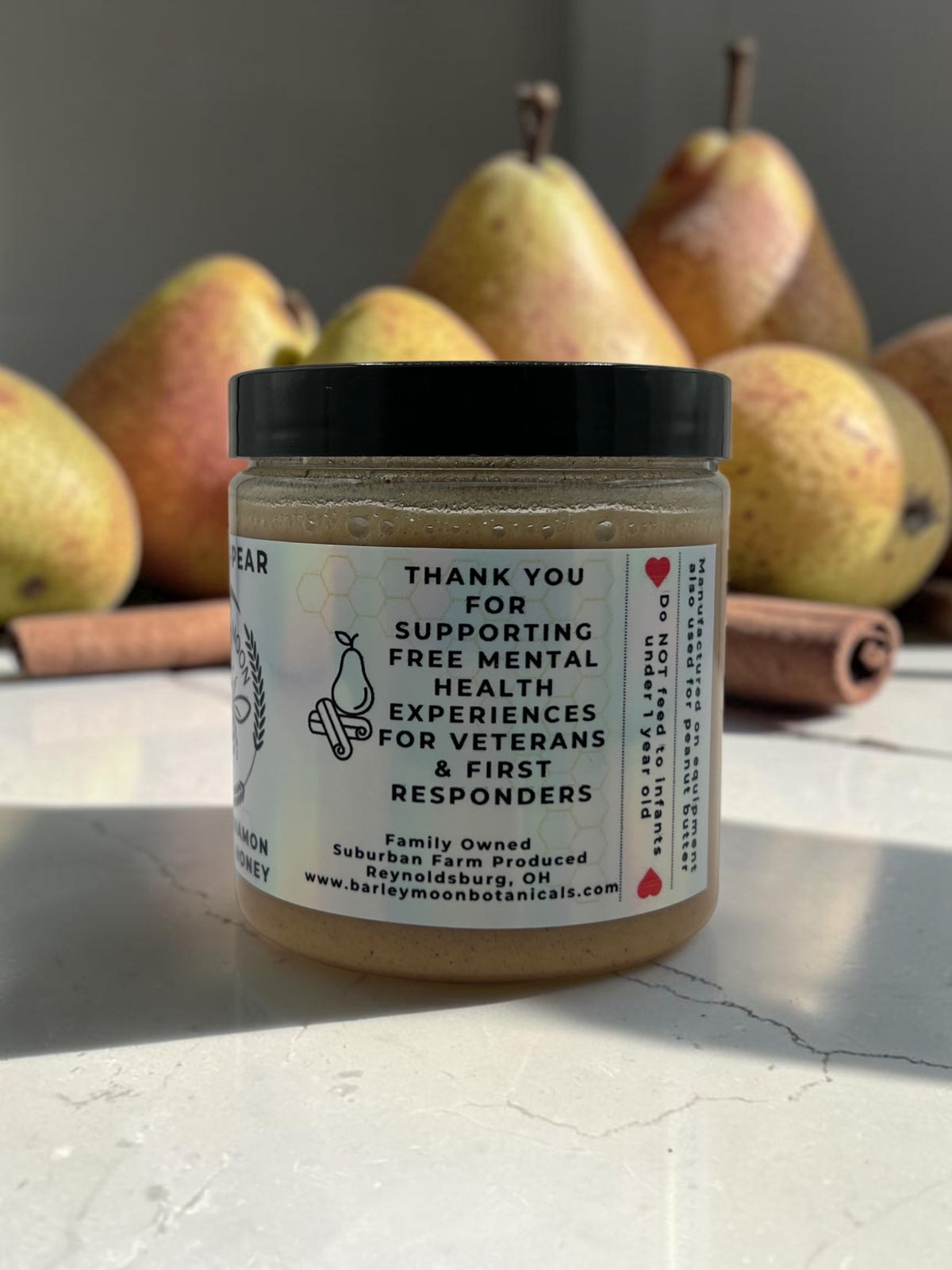 Barley Moon Botanicals Cinna Pear creamed honey jar with fresh pears and cinnamon sticks on a white surface