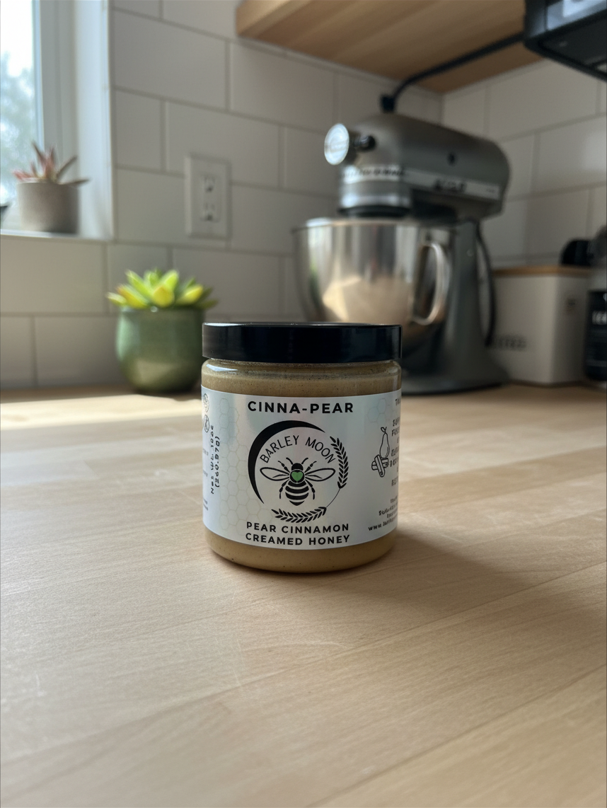 Barley Moon Botanicals Cinna-Pear creamed honey jar on a wooden kitchen counter with a stand mixer in the background.