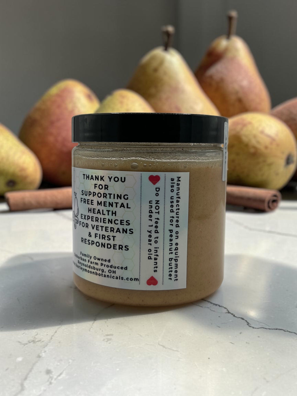 Barley Moon Botanicals Cinna-Pear creamed honey jar with cinnamon sticks and fresh pears on a white surface
