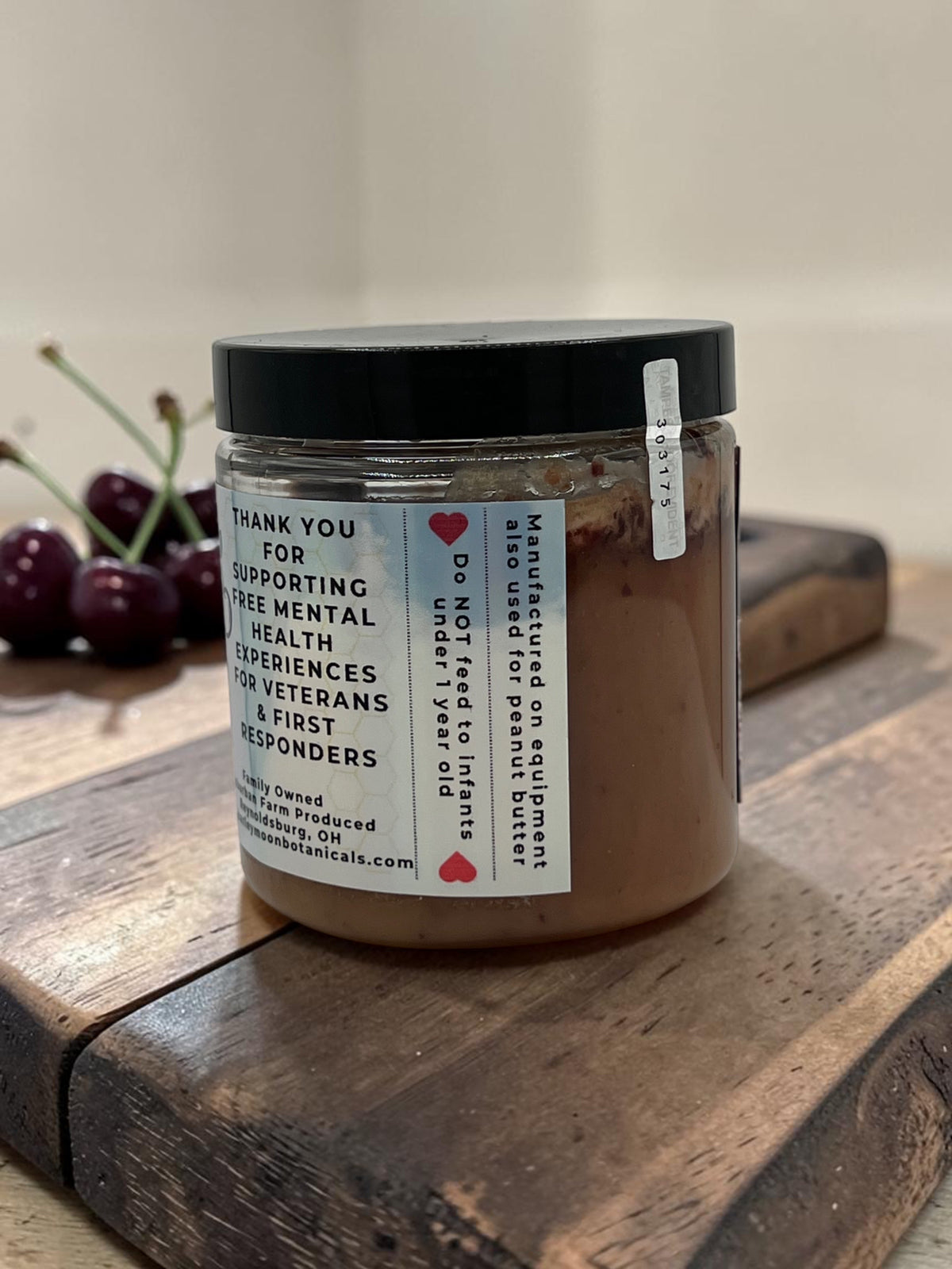 Barley Moon Botanicals Cheery Cherry creamed honey jar on a wooden board with fresh cherries in the background