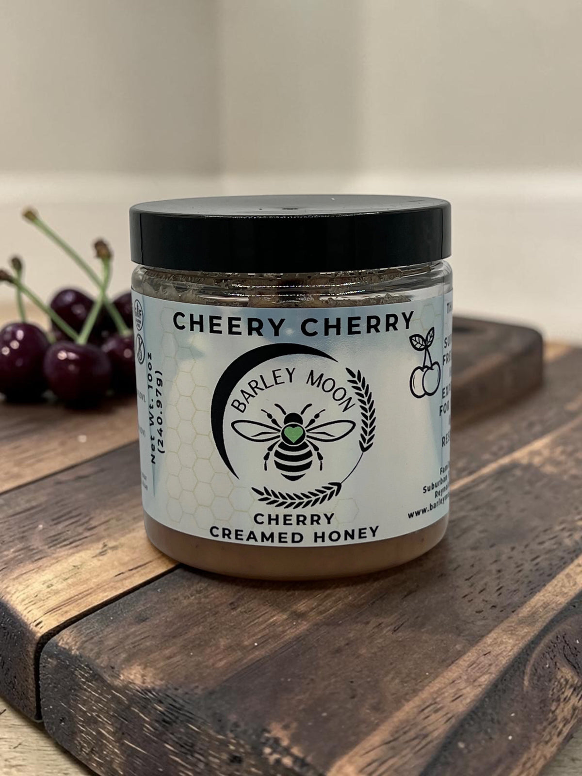 Barley Moon Botanicals Cheery Cherry creamed honey in a glass jar on a wooden board with fresh cherries