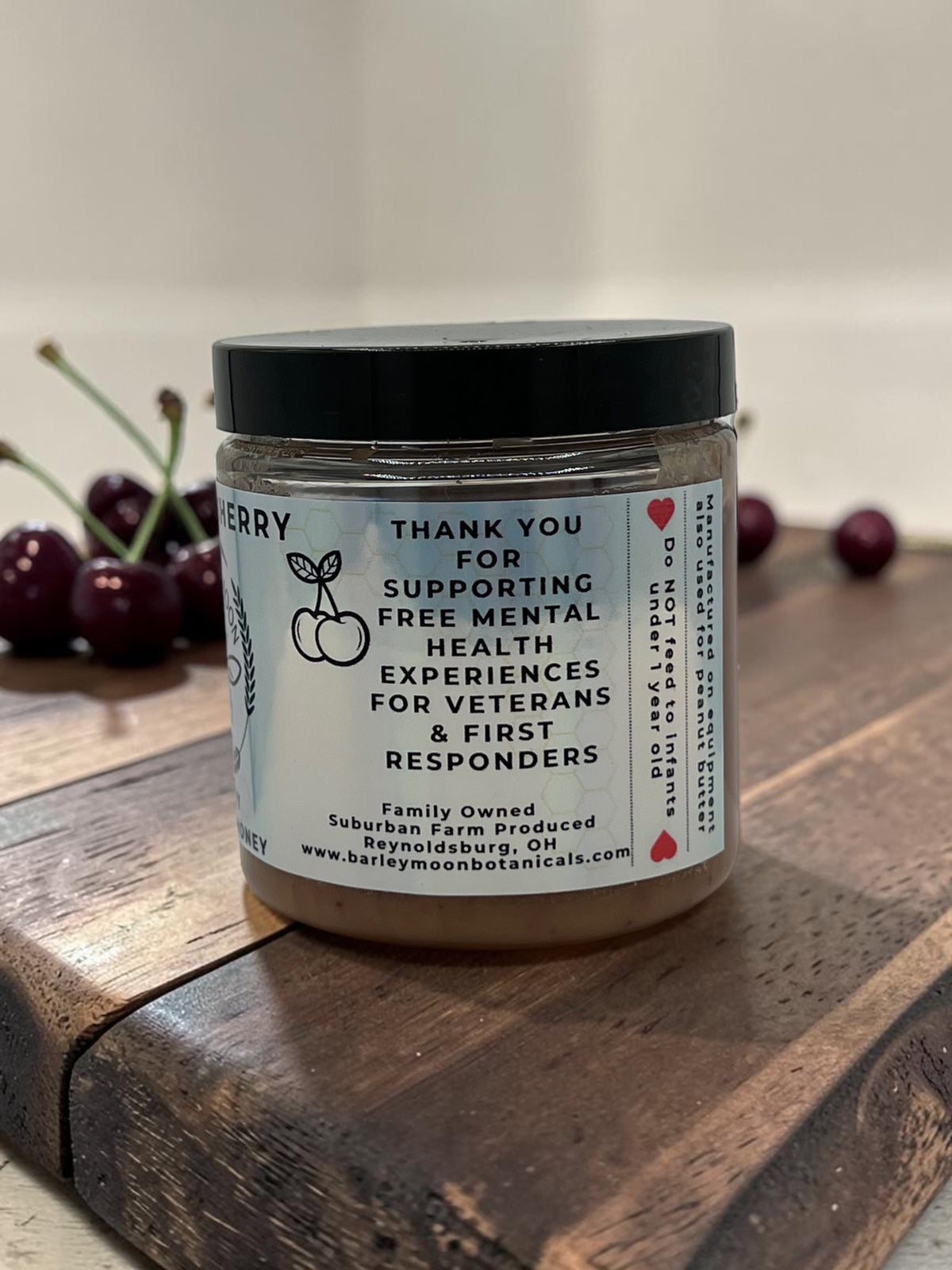 Barley Moon Botanicals Cheery Cherry creamed honey jar on a wooden board with fresh cherries in the background