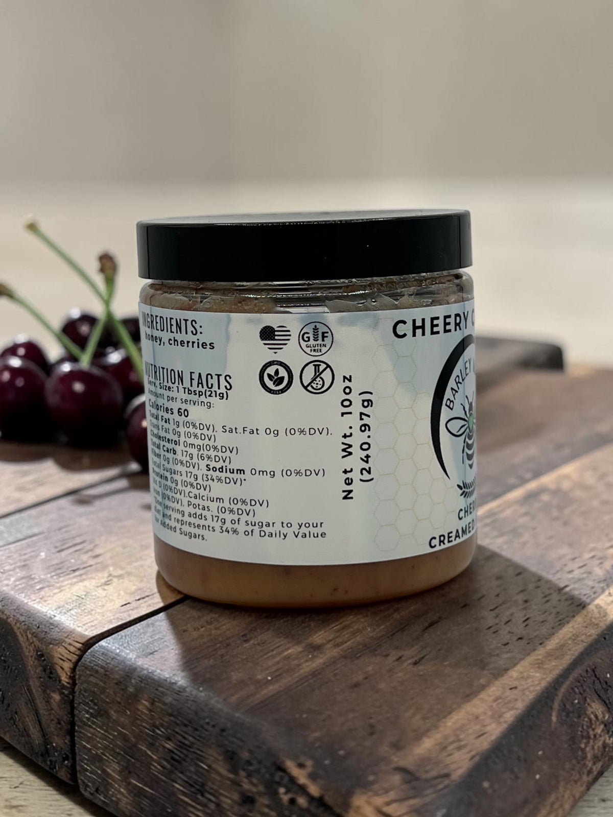 Barley Moon Botanicals Cheery Cherry creamed honey jar on a wooden board with fresh cherries in the background