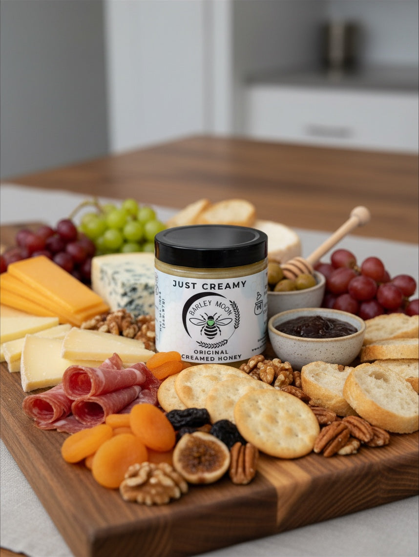 Barley Moon Botanicals Just Creamy original creamed honey jar centered on a gourmet charcuterie board with snacks.