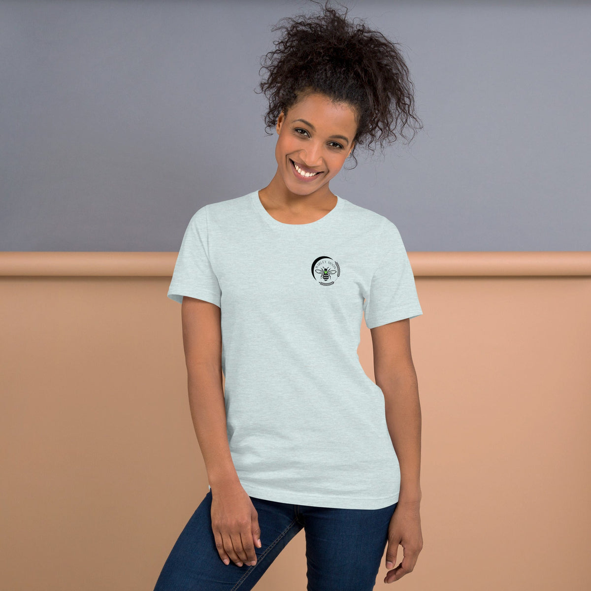 Woman wearing a light grey Barley Moon Botanicals t-shirt with a black bee and crescent moon logo on the chest.