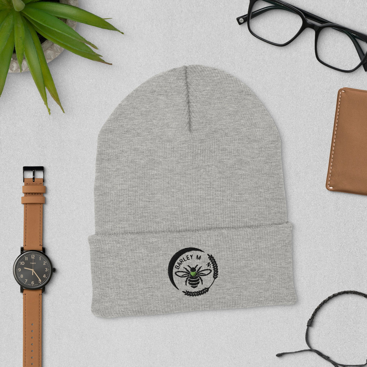 Barley Moon Botanicals grey cuffed beanie with a black bee and moon logo, displayed on a flat lay desk surface.