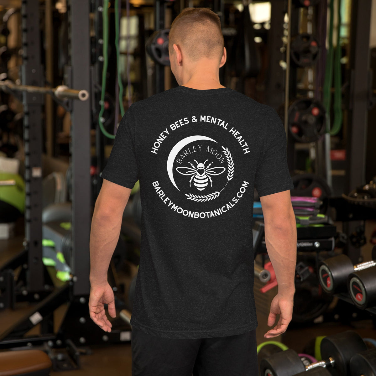 A man wearing a dark grey Barley Moon Botanicals t-shirt with a white bee and crescent moon logo on the back.