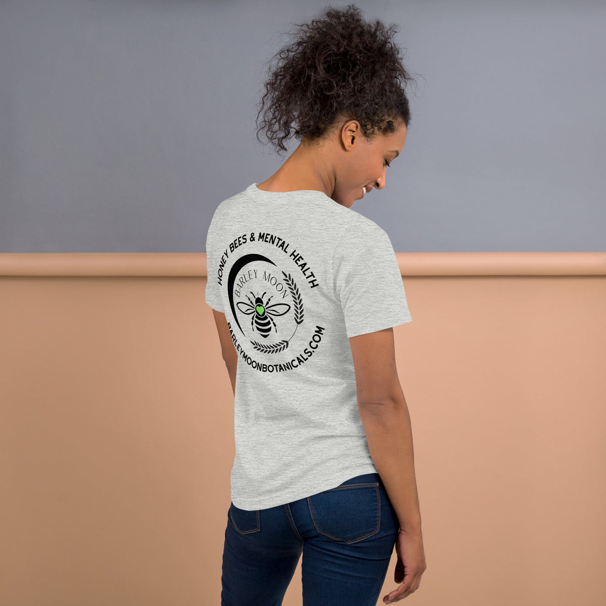 Model wearing a grey Barley Moon Botanicals t-shirt featuring a black bee and crescent moon logo on the back.