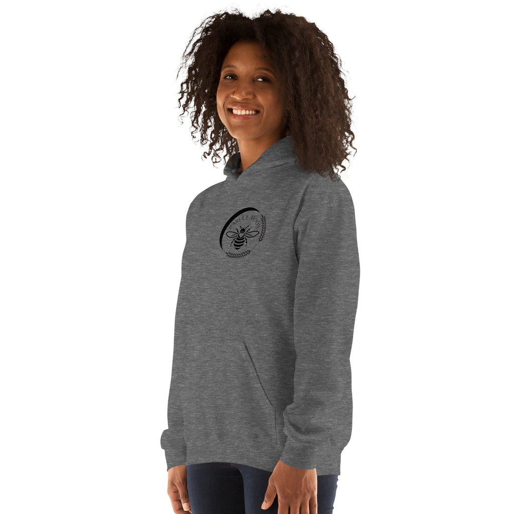 A woman wearing a grey Barley Moon Botanicals unisex hoodie featuring a black bee and crescent moon logo on the chest.