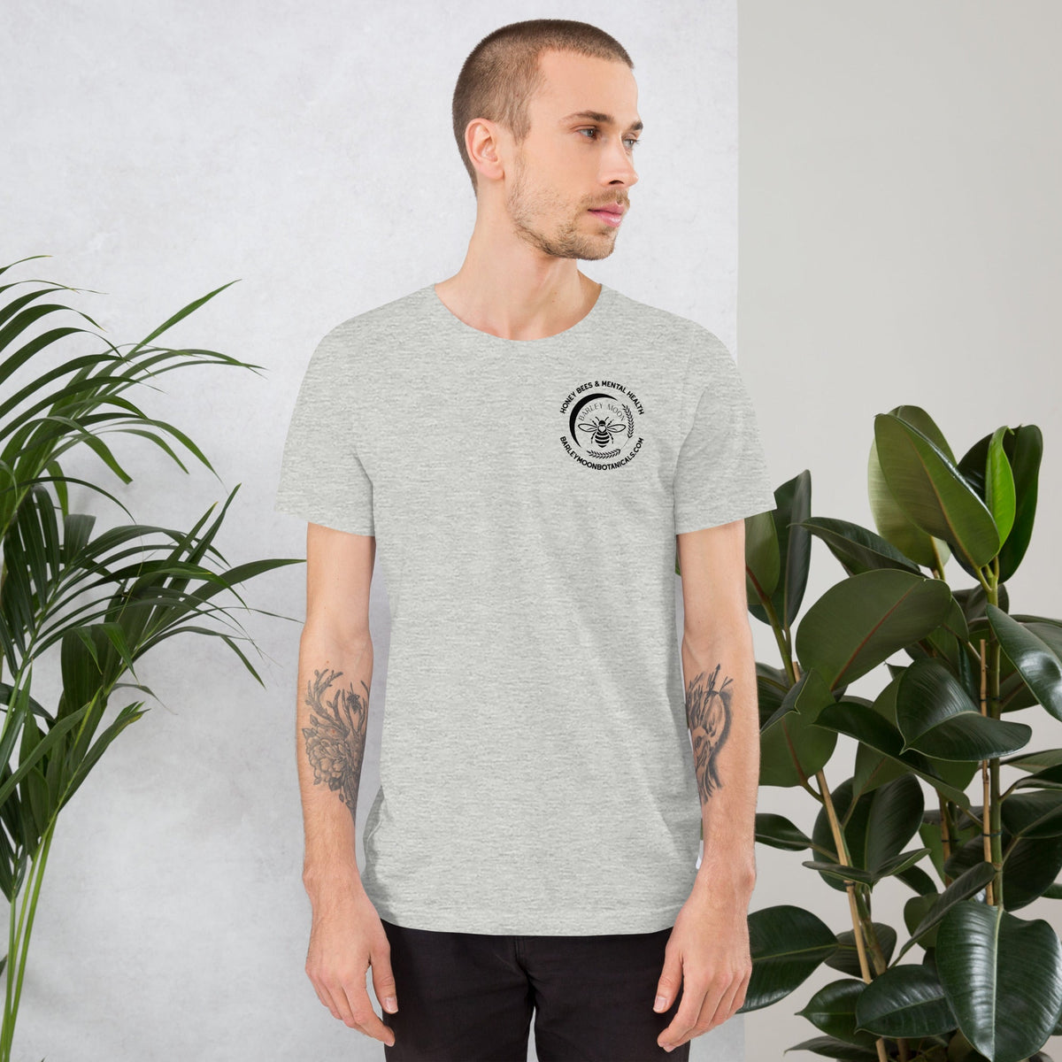 A man wearing a Barley Moon Botanicals grey heather unisex t-shirt with a small bee logo on the chest.