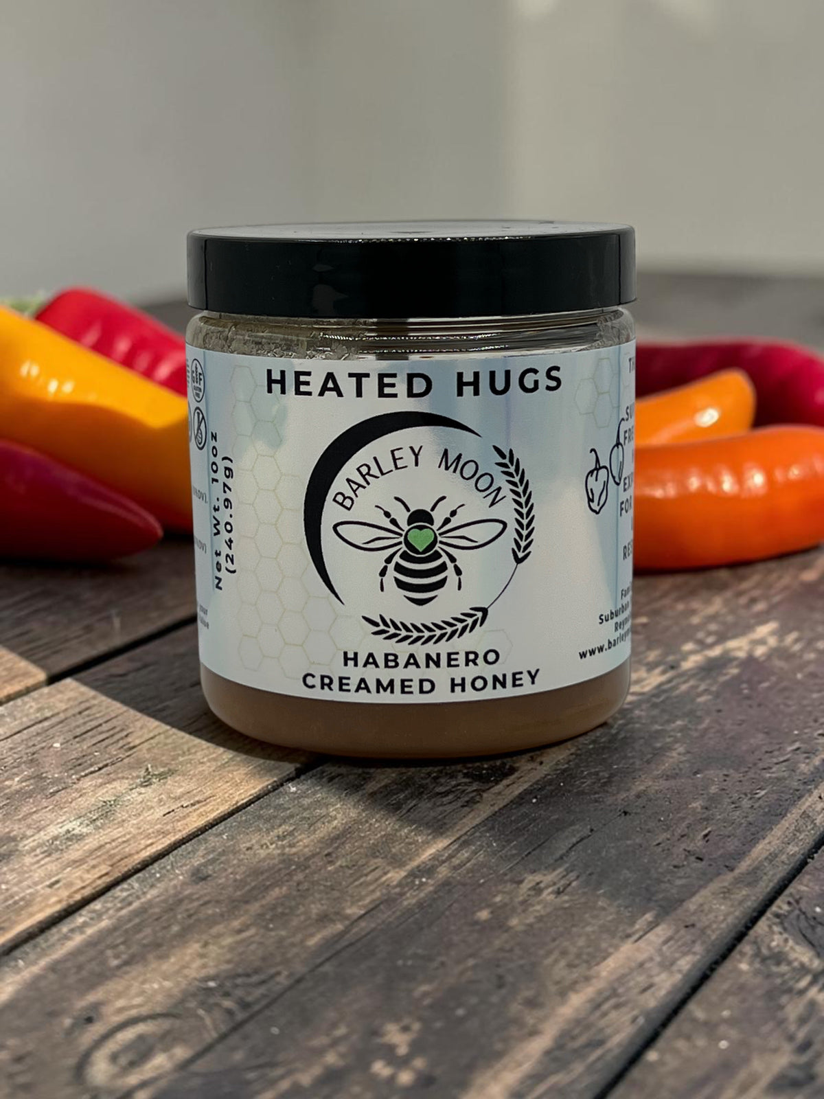 Barley Moon Botanicals Heated Hugs habanero creamed honey in a glass jar with fresh chili peppers on a wooden table.