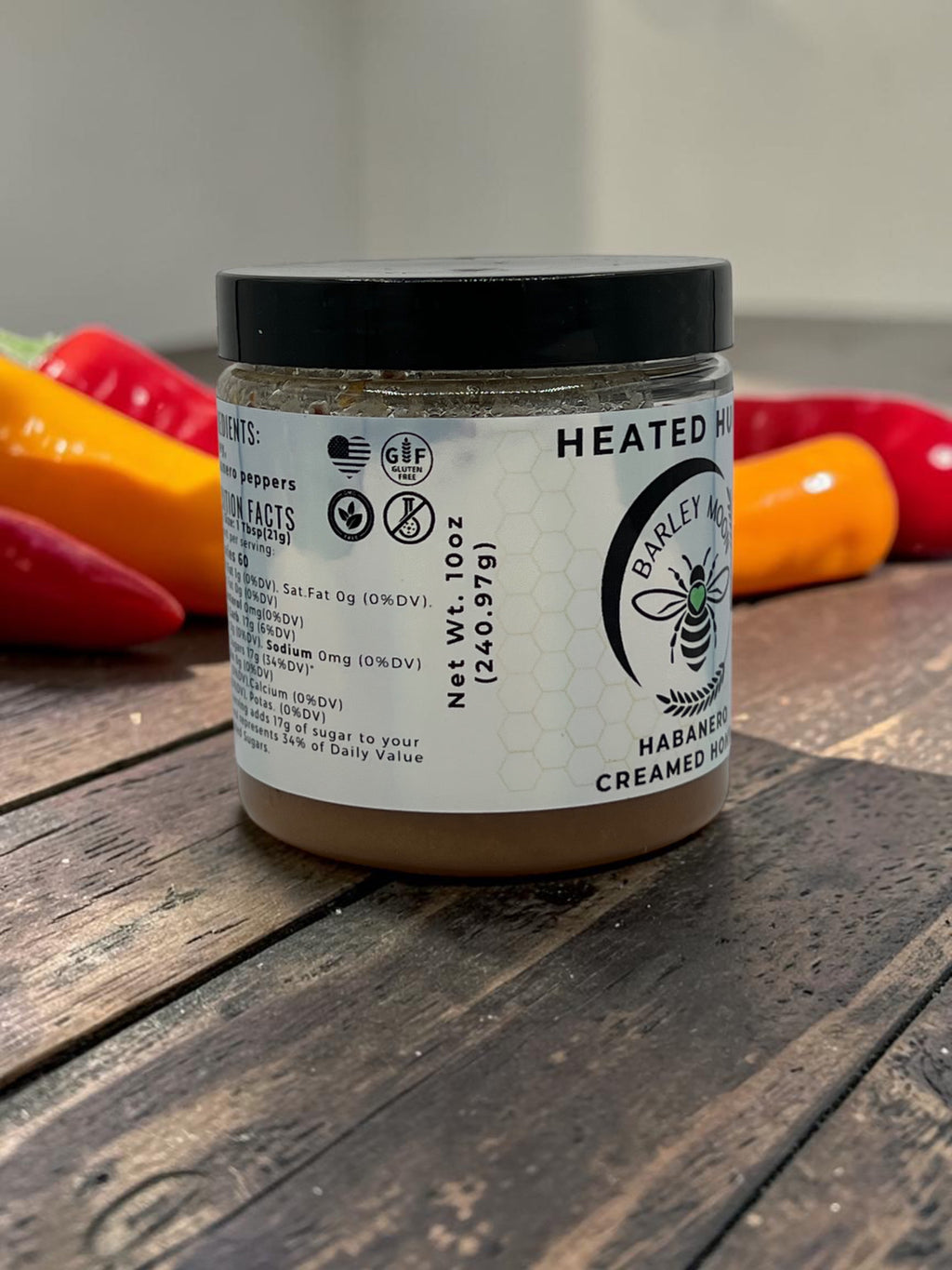 Barley Moon Botanicals Heated Hugs habanero infused creamed honey jar on a wooden surface with fresh chili peppers