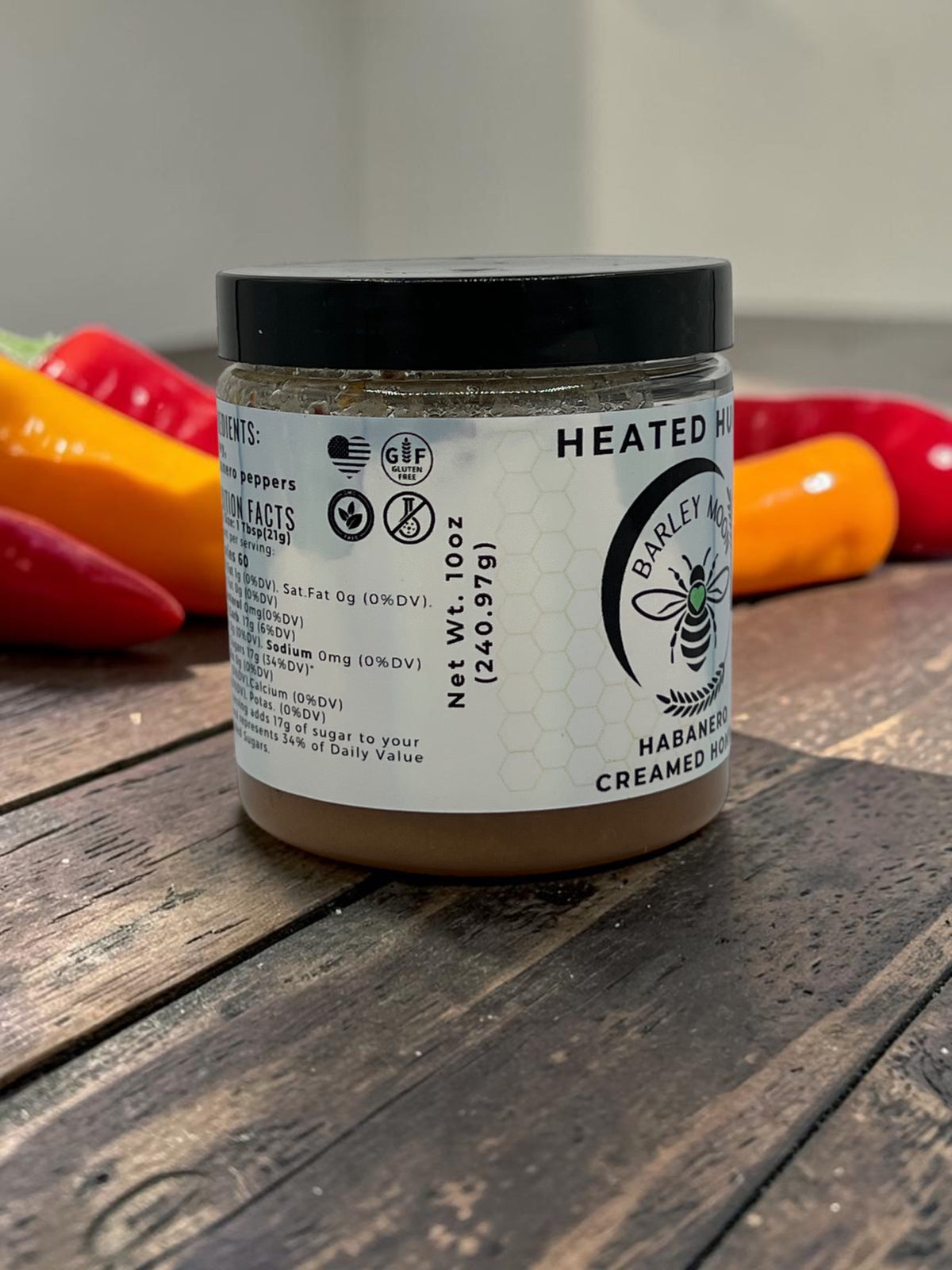 Barley Moon Botanicals Heated Hugs habanero infused creamed honey jar on a wooden surface with fresh chili peppers