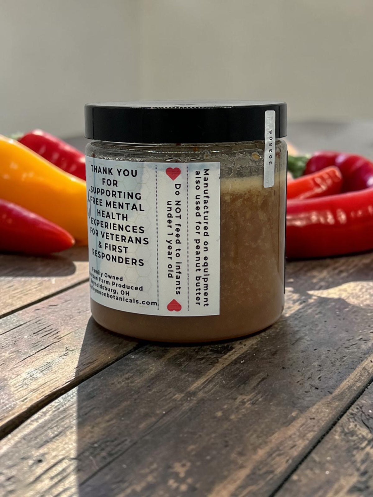 Barley Moon Botanicals Habanero Honey jar with a mission statement label, set against fresh red and yellow peppers.