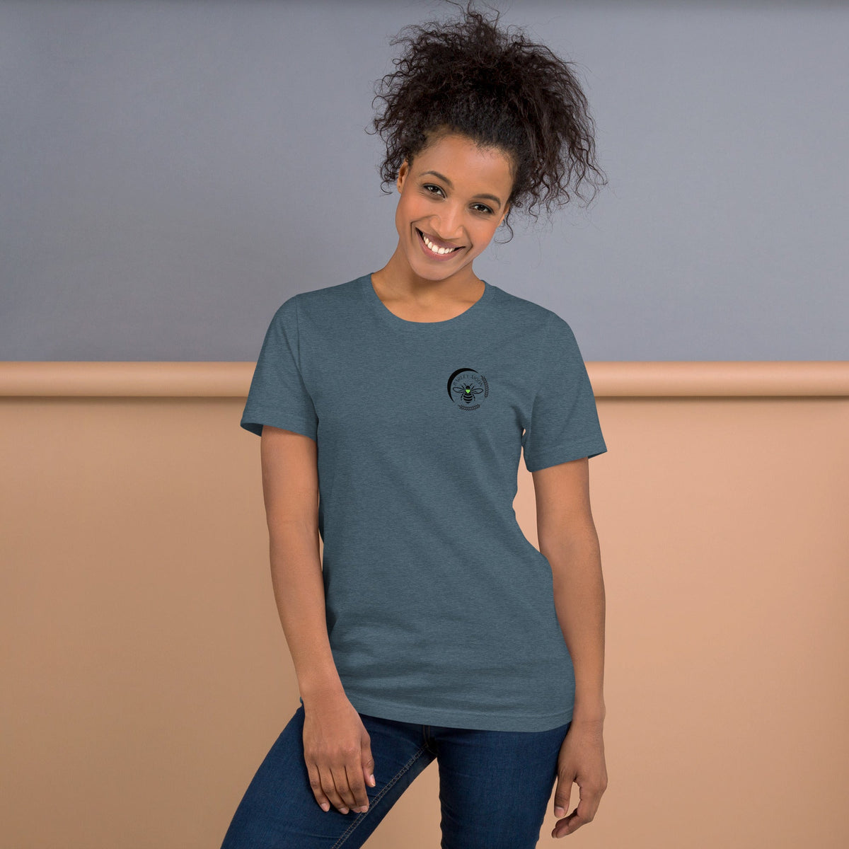 A woman wearing a Barley Moon Botanicals heather blue t-shirt with a black bee and crescent moon logo on the chest.