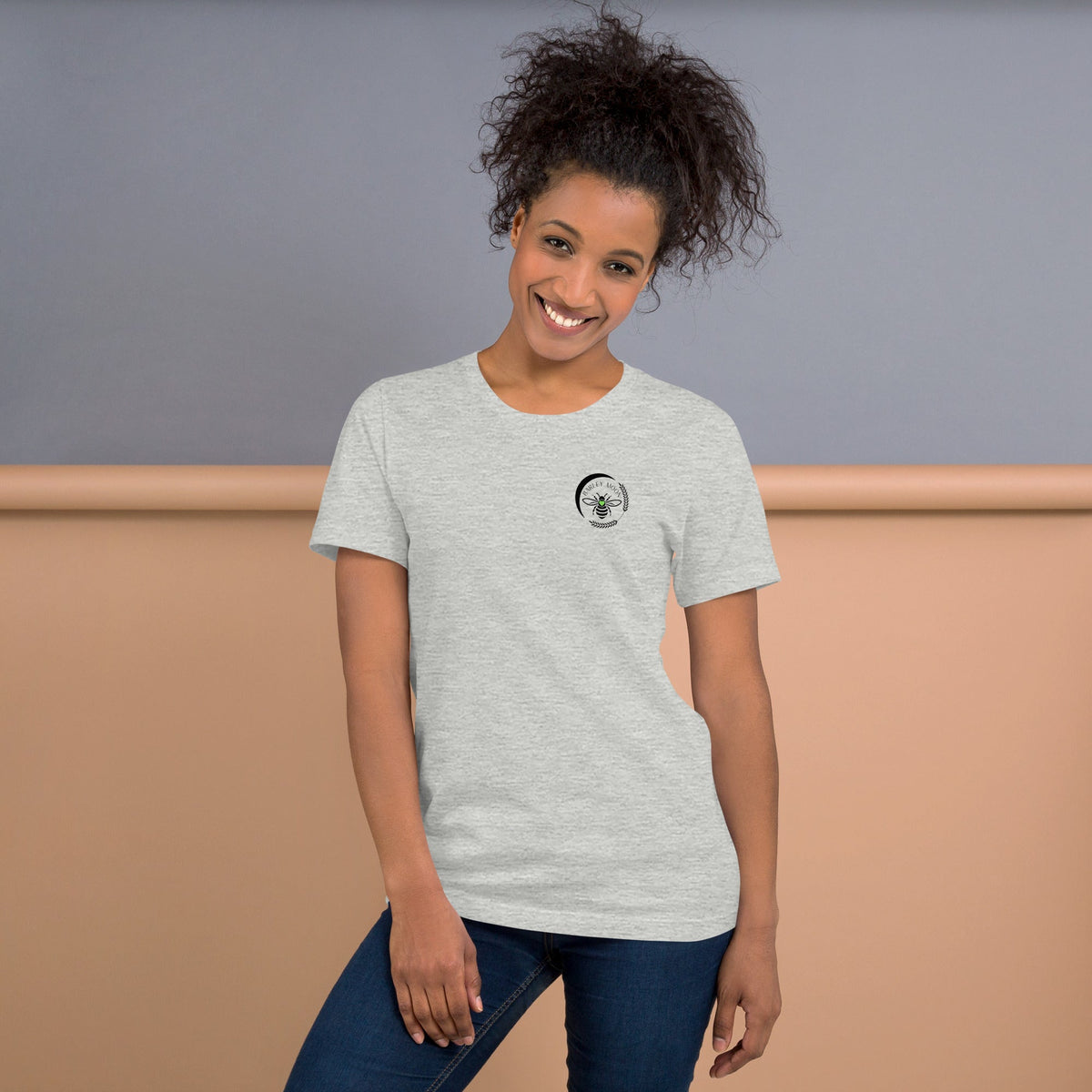 Woman wearing a heather grey Barley Moon Botanicals t-shirt with a black bee and crescent moon logo on the chest.