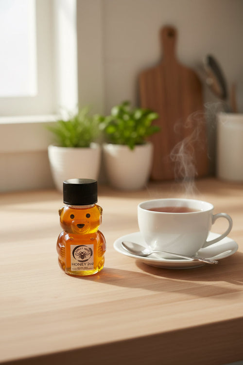 Barley Moon Botanicals 2oz bear-shaped bottle of raw, golden honey sitting on a wooden kitchen counter next to tea.