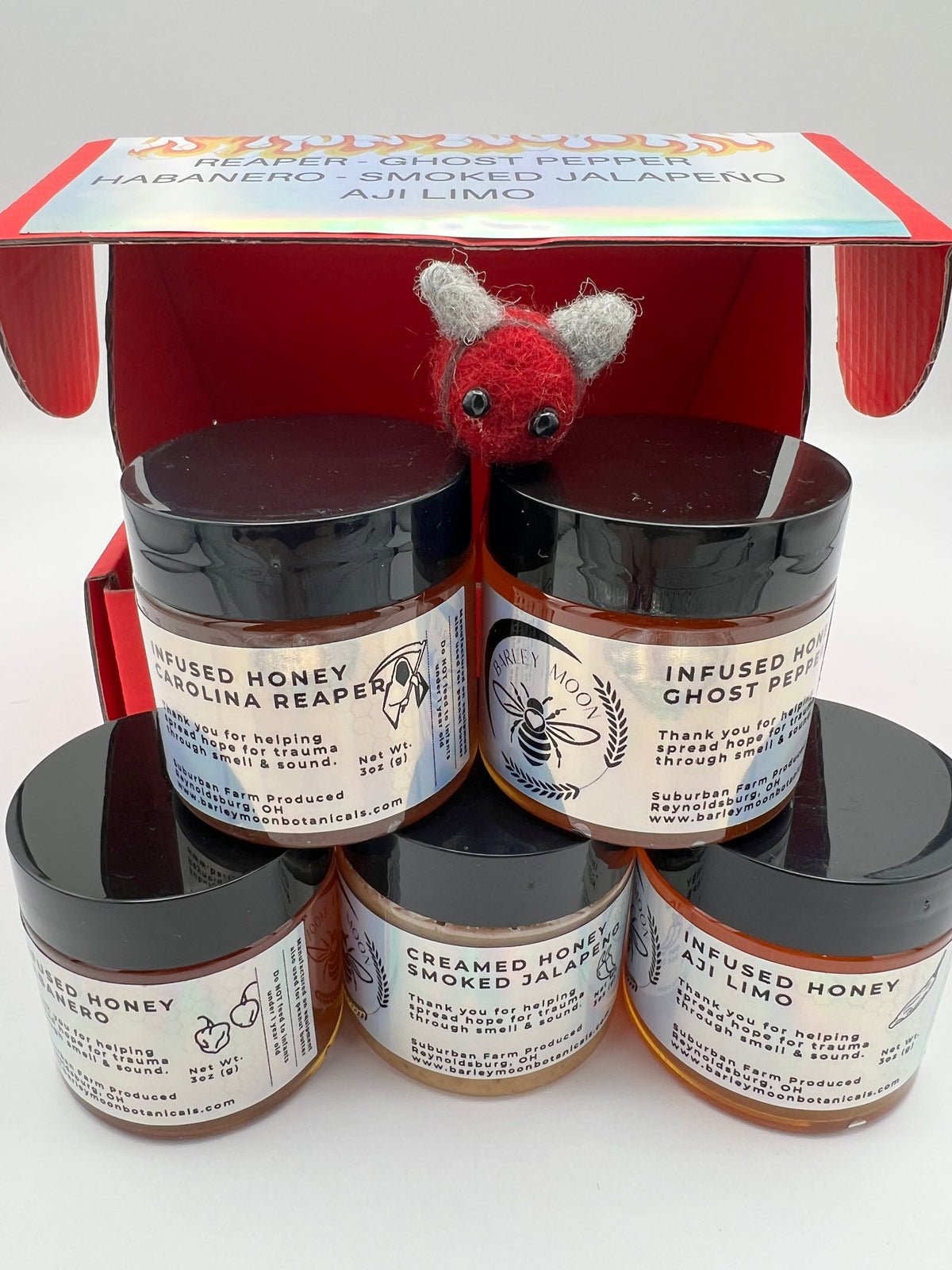 Barley Moon Botanicals Hot Box Honey Flight featuring five jars of spicy infused honey in a red gift box with a felt bee