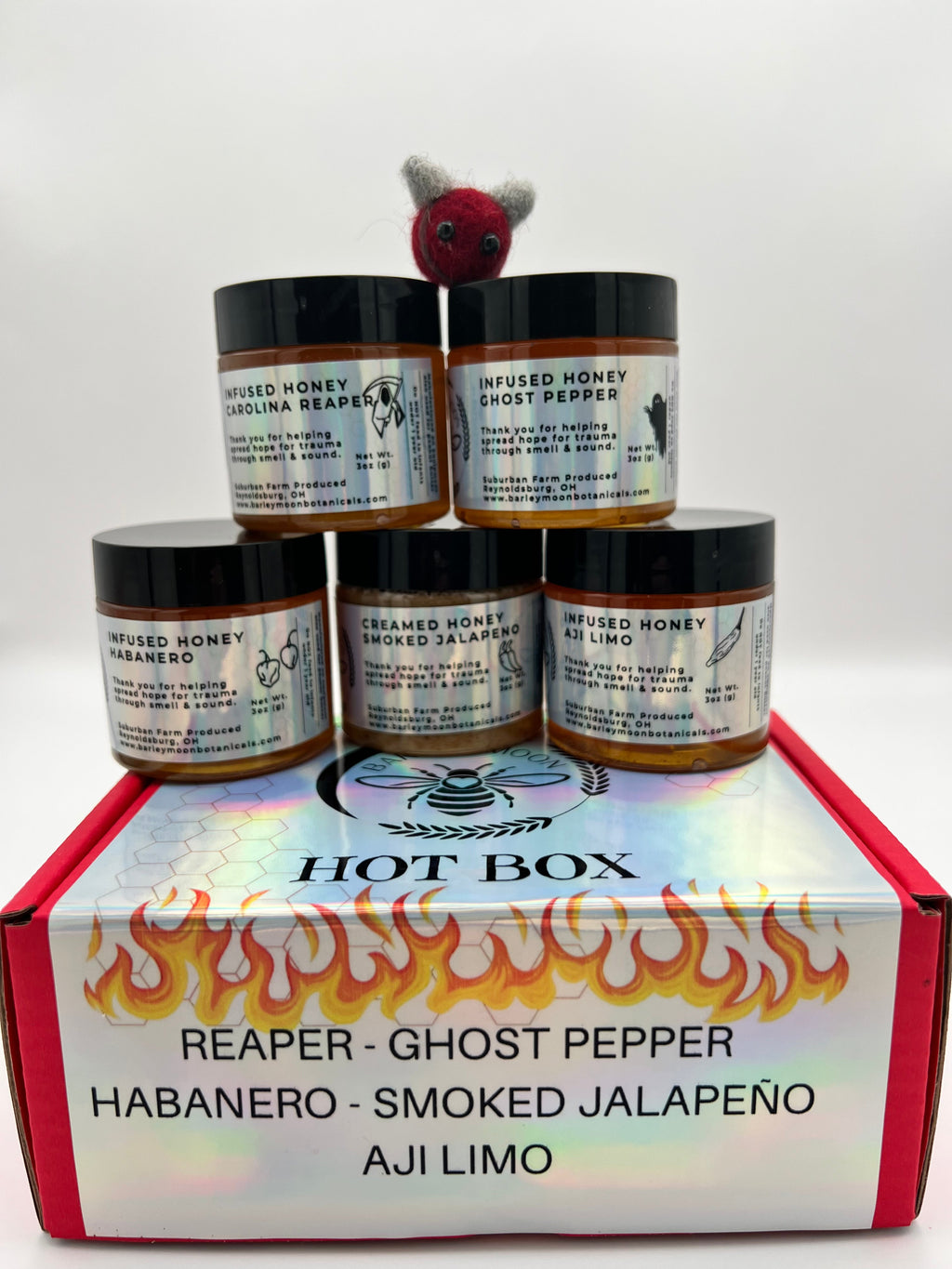 Barley Moon Botanicals Hot Box Honey Flight featuring five jars of spicy infused honey in a red gift box with a felt bee