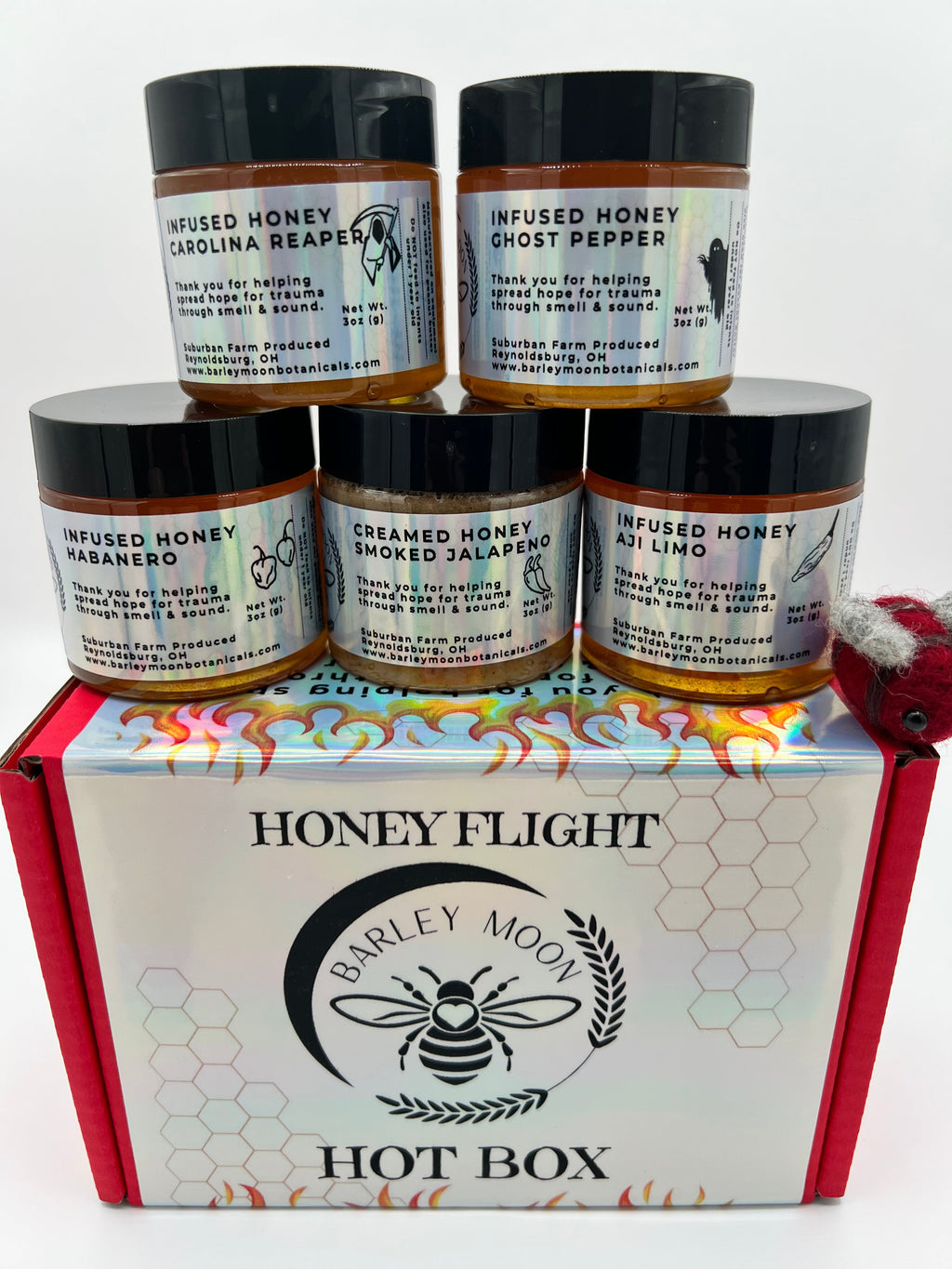 Barley Moon Botanicals Hot Box Honey Flight featuring five jars of spicy infused honey in a red gift box with a felt bee