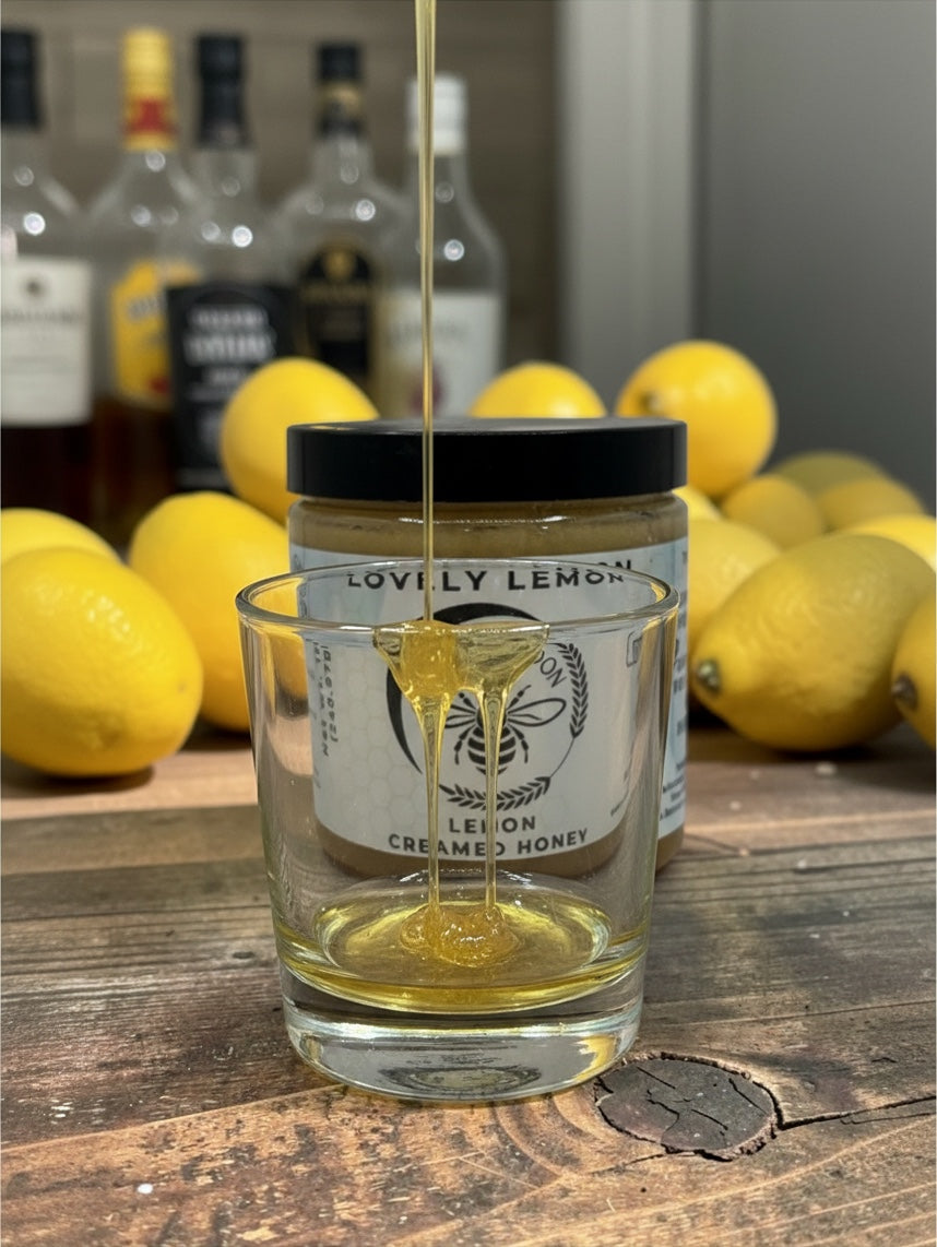 Barley Moon Botanicals Lovely Lemon creamed honey drizzling into a glass with fresh lemons on a rustic wooden table