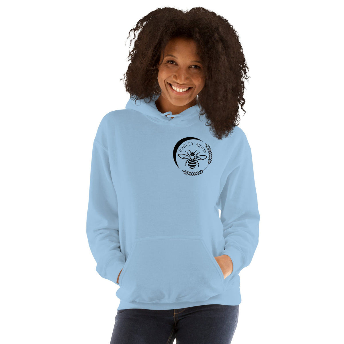 A smiling woman wearing a light blue Barley Moon Botanicals unisex hoodie with a black bee and crescent moon logo.