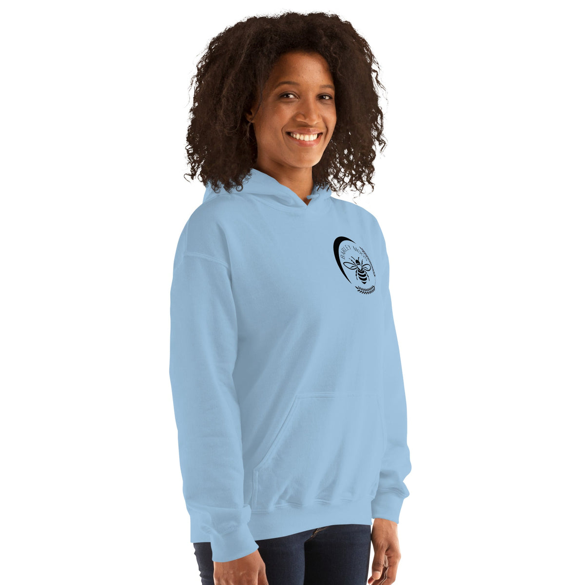 A woman wearing a light blue Barley Moon Botanicals unisex hoodie featuring a black bee and crescent moon logo.