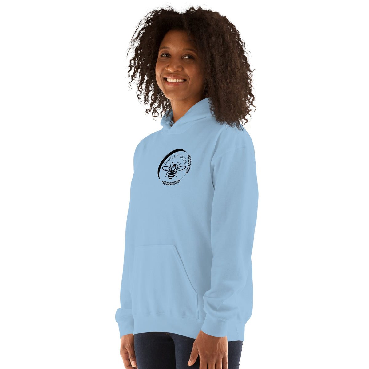 A woman wearing a light blue Barley Moon Botanicals unisex hoodie featuring a bee and crescent moon logo on the chest.