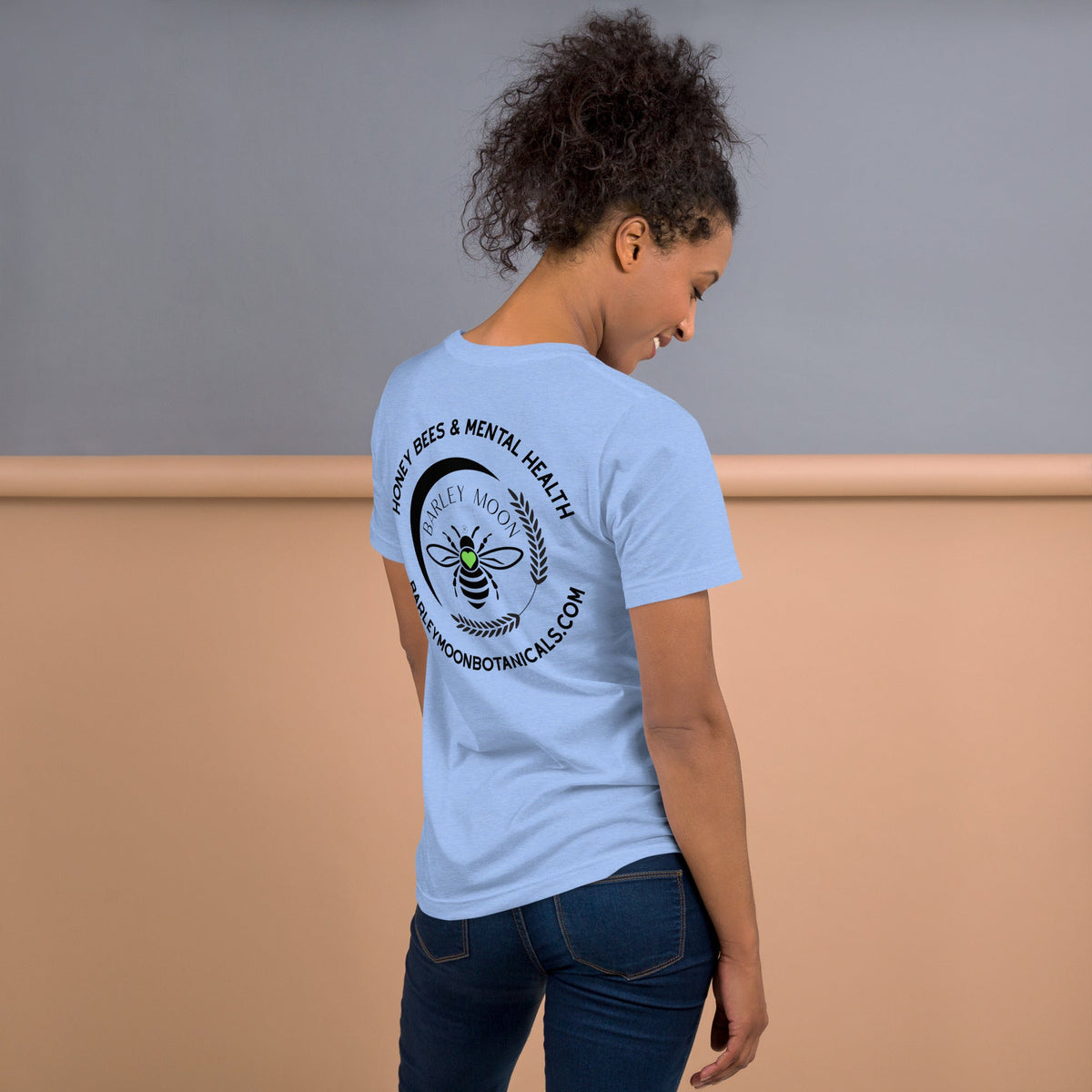 Woman wearing a light blue Barley Moon Botanicals t-shirt with a black bee and crescent moon logo on the back