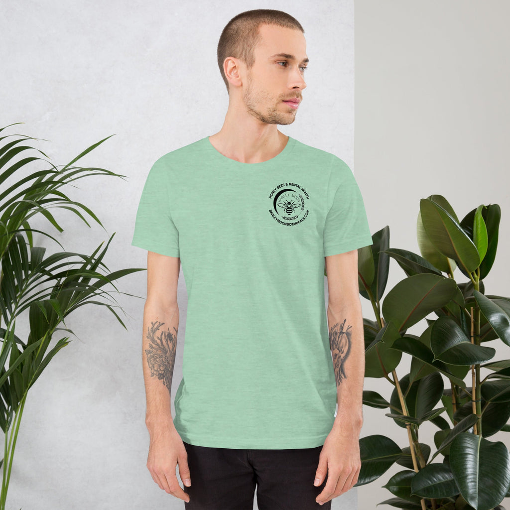 Man wearing a light green Barley Moon Botanicals unisex t-shirt with a small bee logo on the chest in a studio setting
