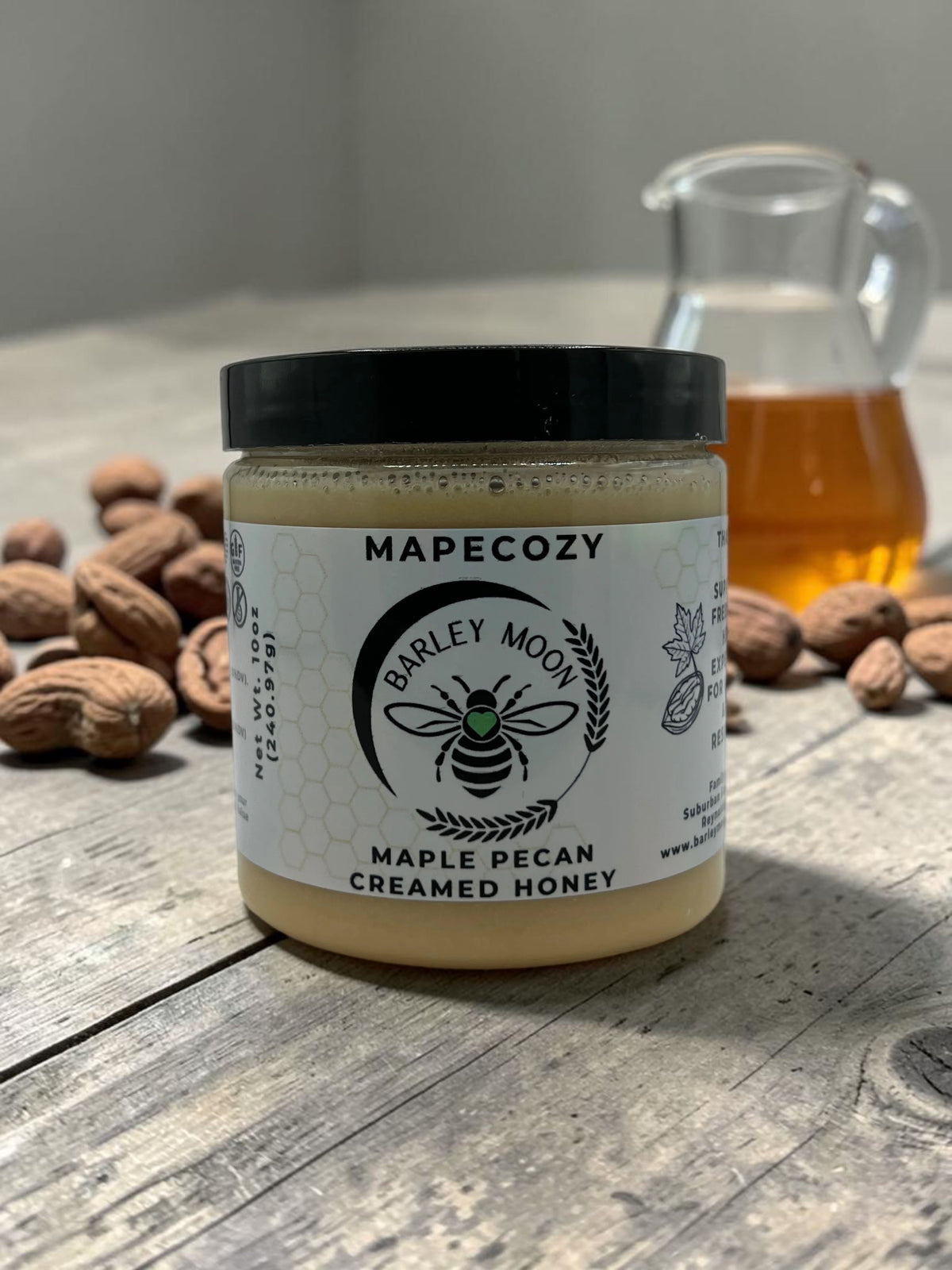 Barley Moon Botanicals MapeCozy maple pecan creamed honey in a glass jar on a rustic wooden table with pecans.