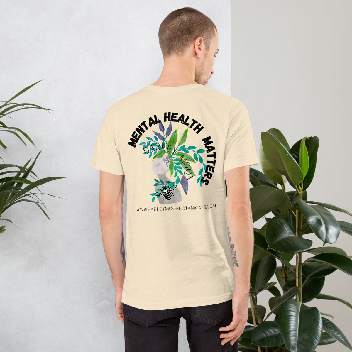 A man wearing a cream Barley Moon Botanicals unisex t-shirt with a botanical Mental Health Matters graphic on the back.