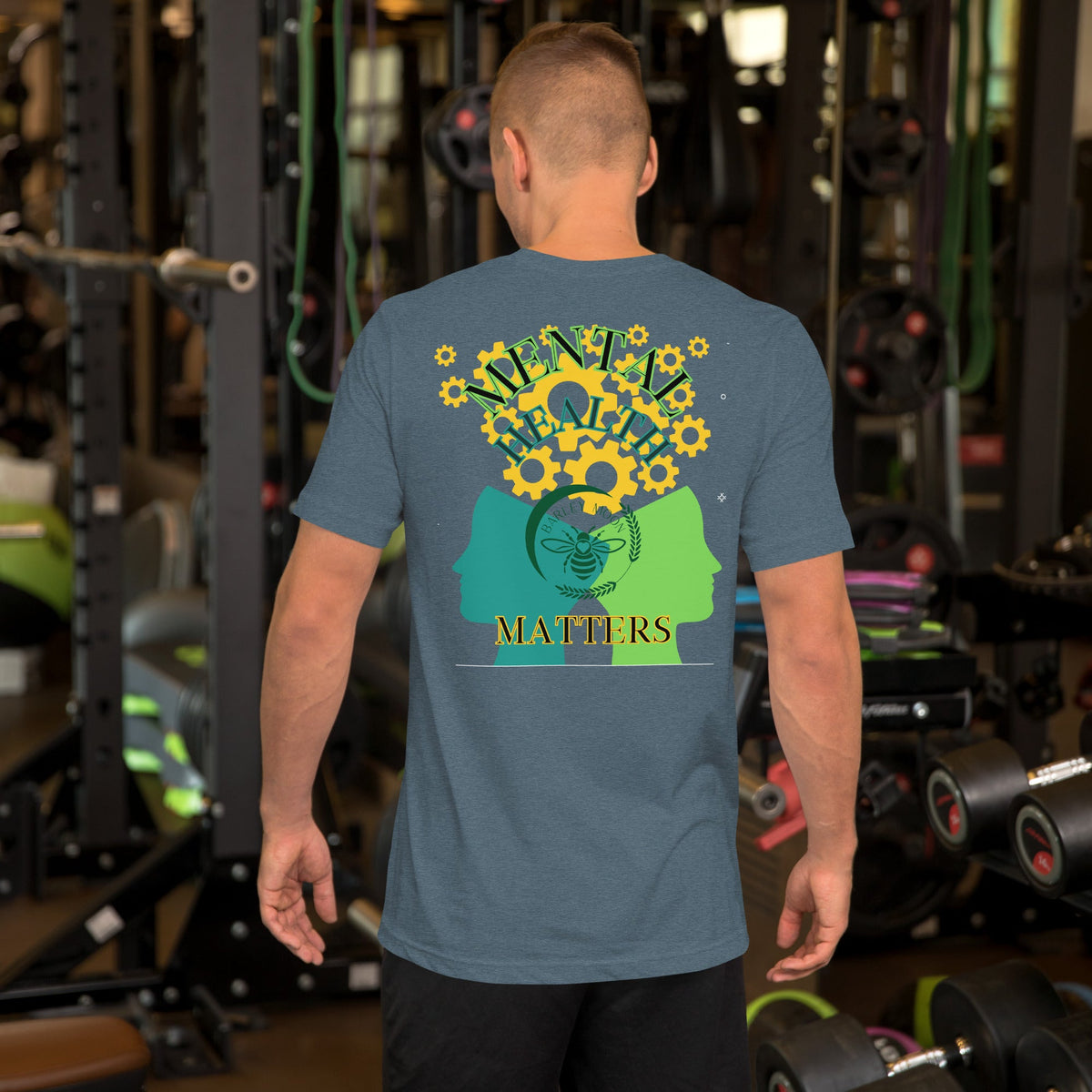 A man wearing a Barley Moon Botanicals heather blue unisex t-shirt with a mental health graphic on the back in a gym.